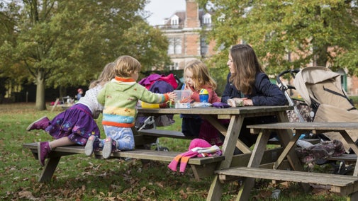 Mother with three young children sitting at picnic table with Sudbury Hall in background